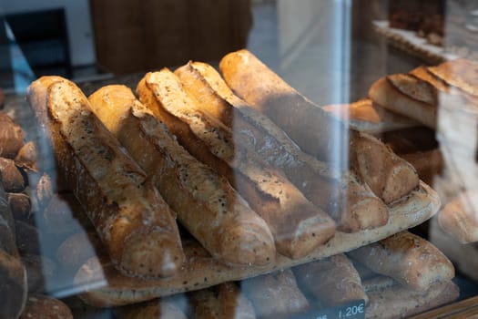 A selection of golden-brown French bread loaves is arranged on a wooden shelf inside a cozy bakery, with natural light casting soft shadows over the crusts.