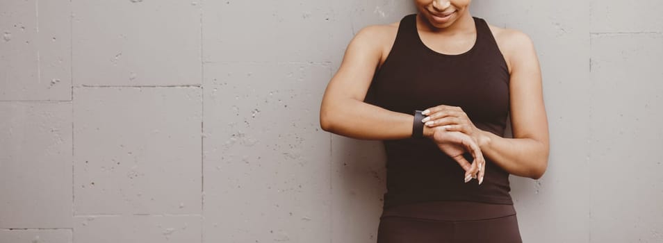 Healthy lifestyle and sport in summer. Smiling african american woman is happy with result of jogging and looks at fitness tracker, panorama, free space