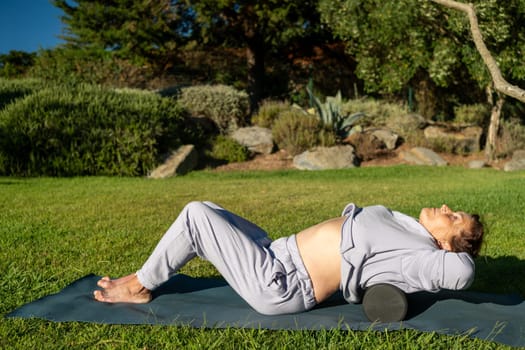 Senior woman releasing her back muscles with MFR rollers at park, enjoying therapeutic and refreshing outdoor workout, enhancing her mobility and wellbeing