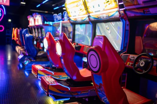 Game Center: Empty red gaming chairs in illuminated arcade game zone. Children's play area in shopping center