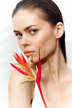 A stunning portrait of a young woman holding a vivid flower, expressing confidence and allure. The minimalist white background enhances her radiant features.