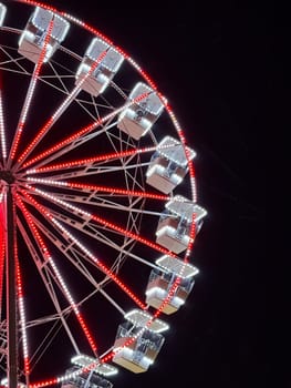 A close-up of a Ferris Wheel illuminated with red and white lights against a dark night sky