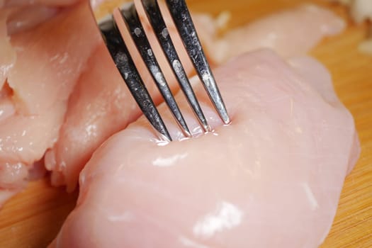 Carefully preparing raw chicken breast by piercing it with a fork.