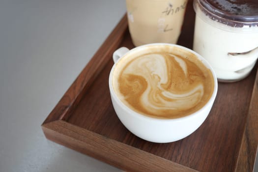 A coffee with lovely foam sits on a tray next to cold drinks.