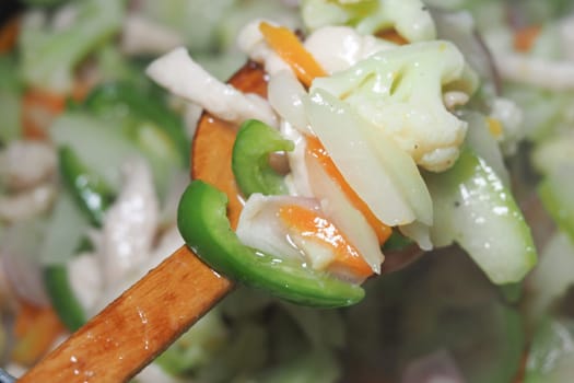 Fresh vegetables being stirred in a wooden spoon in the kitchen.