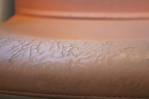 Close-up view of worn leather upholstery on a chair reveals cracks.