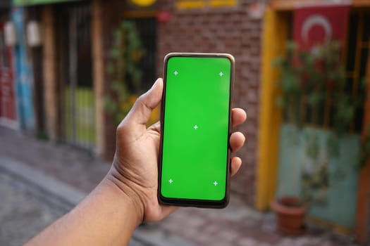 A person shows a smartphone with a green screen on a lively street.