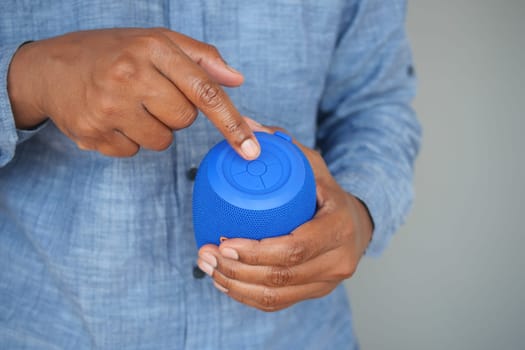 Individual operates a blue wireless speaker while dressed casually.