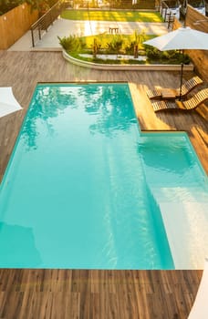 Luxurious turquoise swimming pool with wooden deck, umbrellas, and lounge chairs in a serene backyard setting