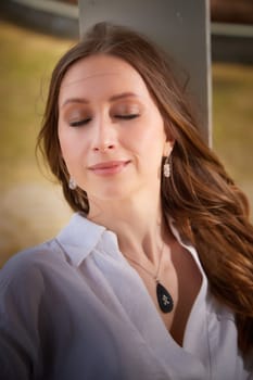 A young woman sits outdoors, eyes closed, soaking in the sunlight and enjoying tranquility in nature.