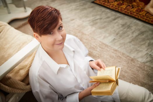 Woman with short hair reads a book while sitting comfortably in a warm, inviting room.