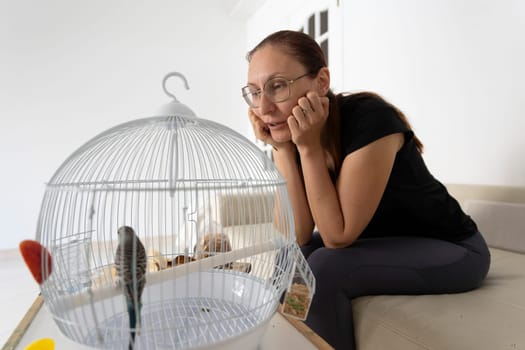 Woman admiring her pet parrot inside its cage in the living room