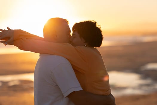 Couple kissing and embracing on beach at sunset, enjoying a romantic moment together