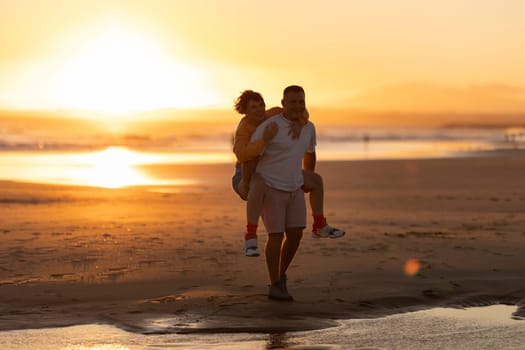 Couple having fun piggybacking on the beach at sunset, enjoying summer vacation together