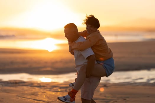 Man giving piggyback ride to woman on beach at sunset, enjoying summer vacation