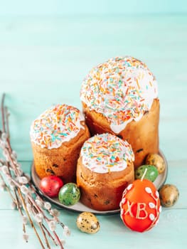 Traditional Russian Ukrainian Easter Cake Kulich. Orthodox Christian Easter Bread or Easter Cake with frosting, Easter Eggs and willow twigs on blue background. Copy space for text, vertical