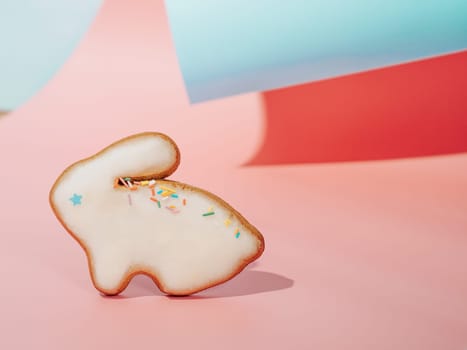 Easter bunny cookie on pink and blue curved paper pastel background with shadows. Happy Easter Day concept. Minimal Easter concept. Copy space. Easter cooking baking background.