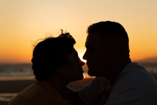 Silhouette of romantic couple touching noses on beach at sunset, enjoying intimacy and love
