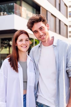 young man and woman smiling happy looking at camera in front of a building, concept of family home and real estate
