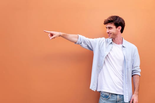 smiling young man in white shirt and blue jeans is pointing to the side, copyspace for text
