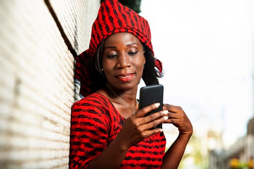 beautiful adult woman in red loincloth standing near a wall looking at her mobile phone while smiling.