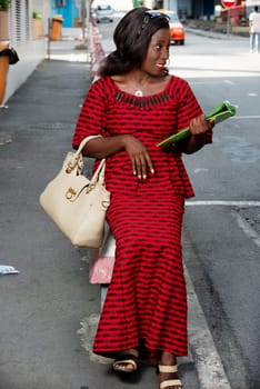 beautiful african adult woman sitting in red loincloth on the street, holding in hand a green document with a beautiful looking sourrie side