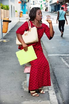 businesswoman in red dress holding a bag and documents, sitting on a concrete wall on the side of the road, off offices drinking bottled water