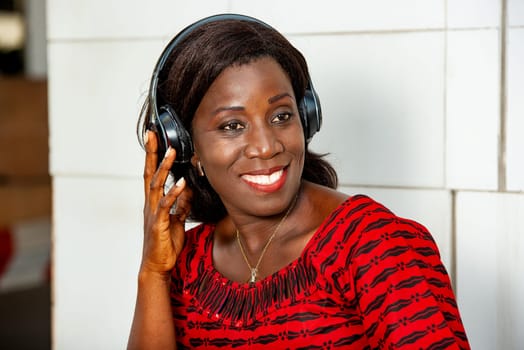 beautiful African adult woman under a beautiful red loincloth, is having fun listening to music in the street, with a headset earplug smiling