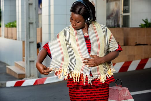 beautiful adult businesswoman dressed in red loincloth, admire her pretty scarf around her neck, in the street while listening to music in her headset