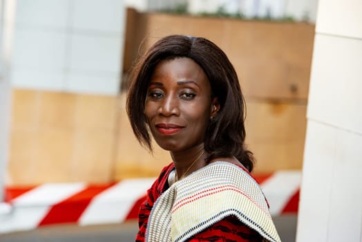 mature african woman in traditional outfit standing outdoors looking at camera smiling.