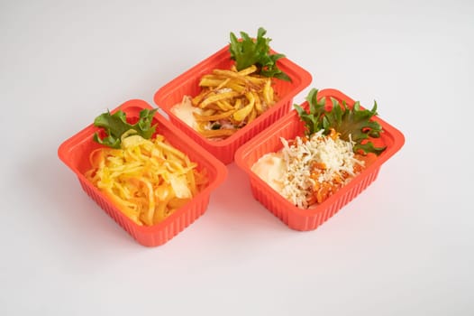 Three red plastic containers holding an assortment of salads and fries with garnishes, for takeaway or ready-to-eat meals.