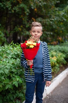 A young pupil boy in stylish clothing holds a bouquet of red and yellow flowers, on September 1 for Knowledge Day, the beginning of the school year
