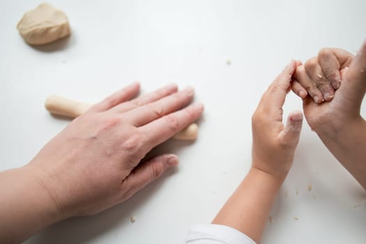 Caucasian adult and child hands working with dough on white surface.