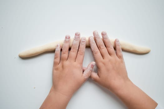 Child hands rolling dough on white surface in baking activity.