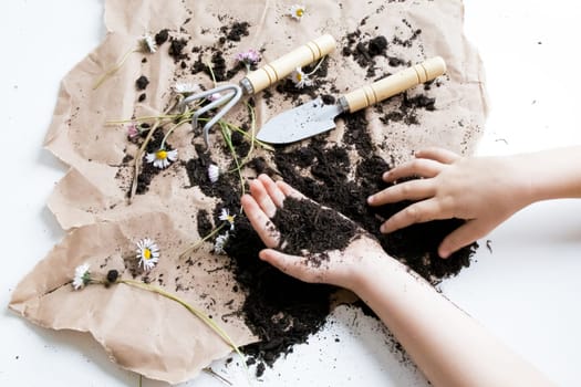 Childrens hands gardening with soil and tools on brown paper with flowers.