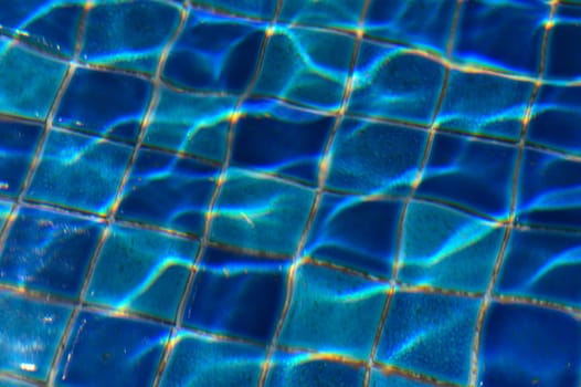 Sunlight glimmers through clear water, creating mesmerizing patterns on the cool blue tiles below, inviting relaxation.