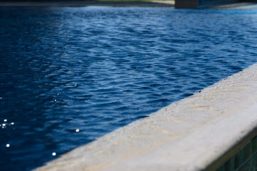 Calm ripples dance on the vibrant water surface, reflecting sunlight at a serene poolside oasis in summer.