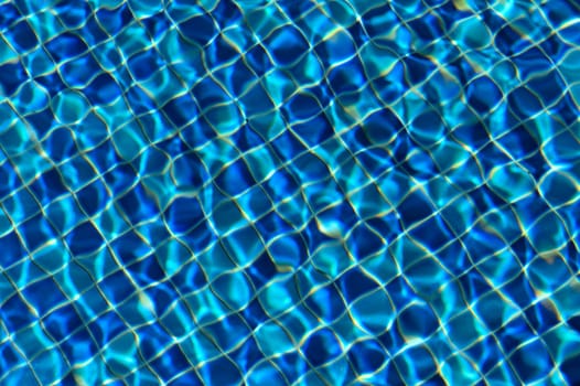 Gentle waves ripple across the deep blue surface of a pool, reflecting sunlight and creating mesmerizing patterns.