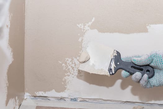 Man plastering wall with putty-knife. Fixing wall surface and preparation for painting.