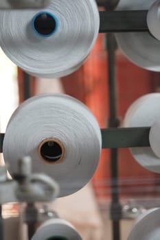 Spools of white thread rotate on machinery in a textile factory.