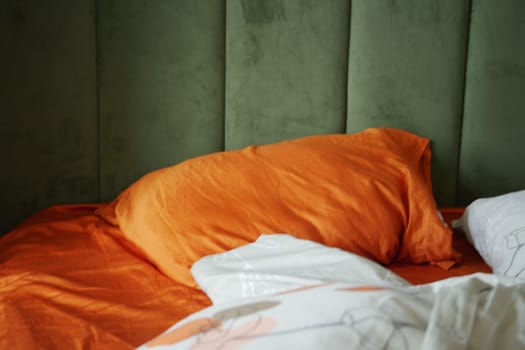 messy bedroom with orange pillow on neatly arranged bed.