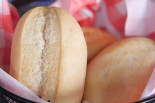 Soft bread rolls are presented in a basket lined with checkered paper.