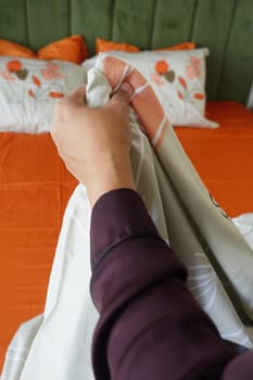 A person adjusts bedding on an orange-colored bed with floral accents.