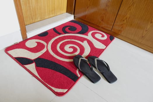 A colorful doormat with flip flops placed at a home's entrance.