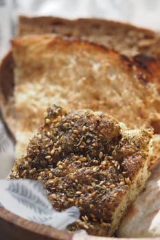 Warm bread topped with herbs and sesame seeds placed in a wooden bowl.
