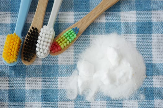 Colorful toothbrushes and baking soda arranged on a textile surface.