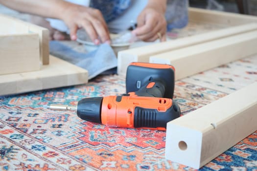 A person assembles wooden pieces using a power drill and tools.