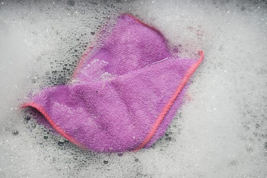 A purple cleaning cloth soaked in soapy water, ready for dishwashing.