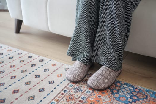 A person relaxes on a couch with feet on a colorful rug.