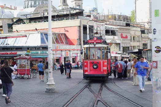 A red tram approaches a bustling area filled with people and shops.